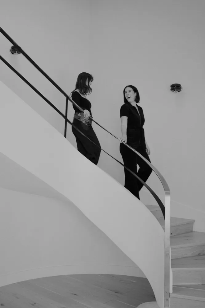Lexi and Delana walking down a curved white staircase, in black and white