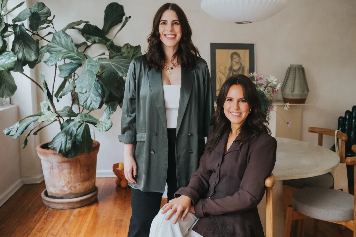 Lexi and Delana in a bright room beside a large potted plant